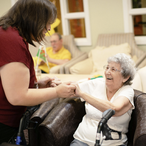Younger woman holding the hands of an older woman. Both are smiling.